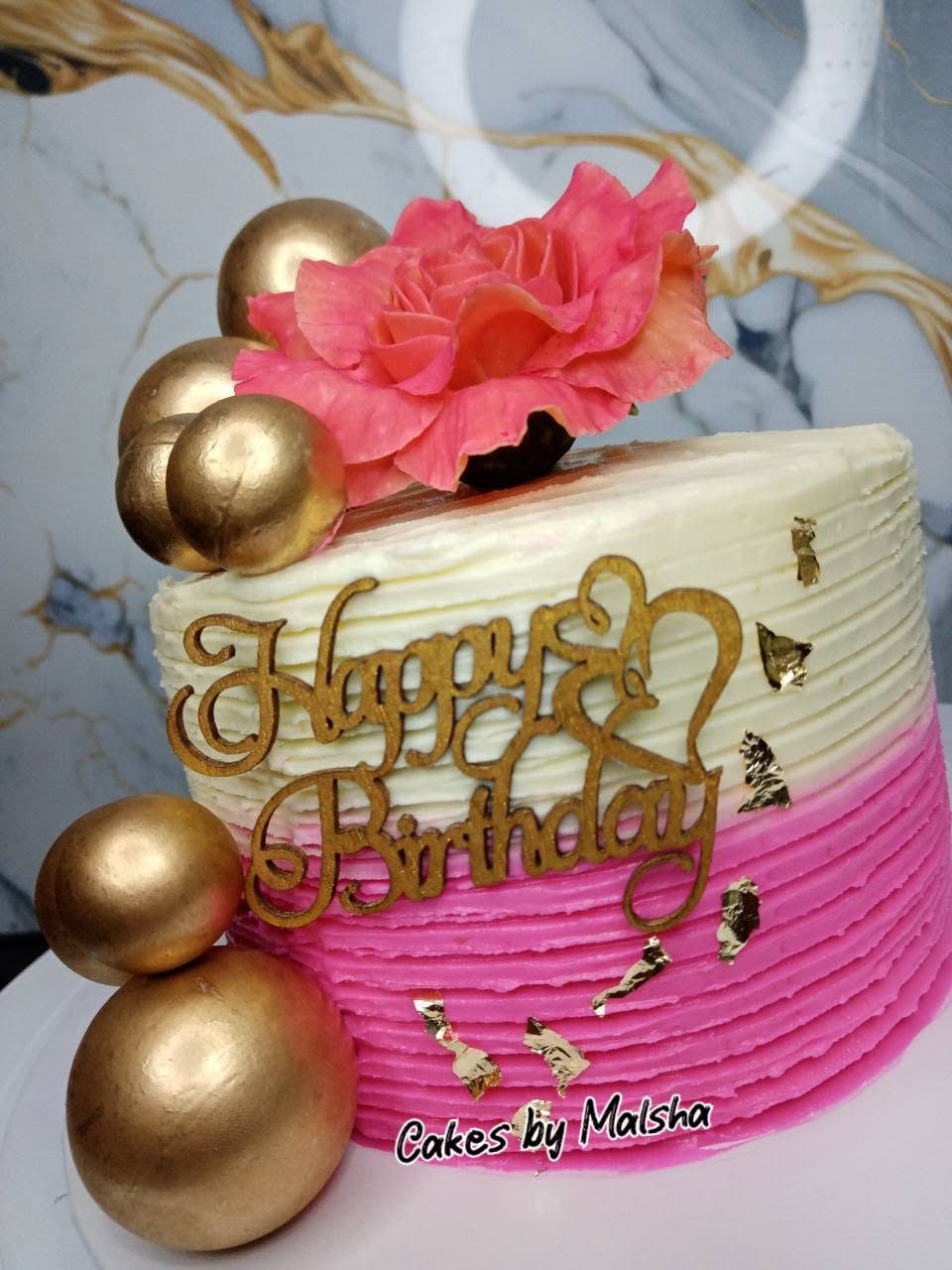 Pink and cream birthday cake with gold spheres and sugar roses